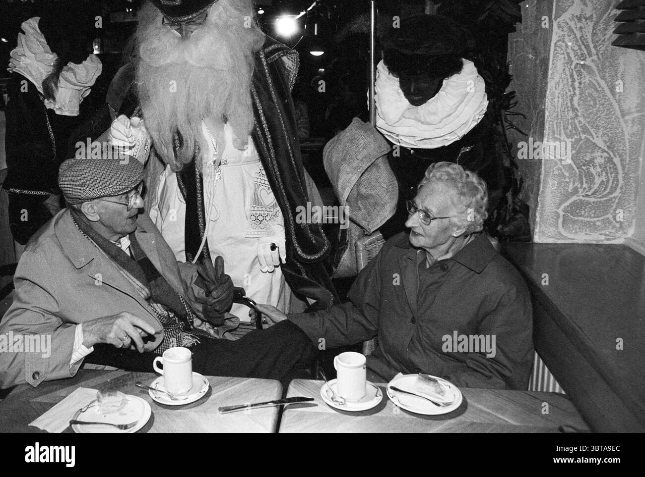 Behinderte kaufen bei V&D, Whizgle News, Dutch Desk, Niederlande, 1950 - 2000 unter 20-11-1995. Diese Themen werden in der Abbildung angezeigt. Die Umgebung ist ein gemütlicher Innenbereich, vielleicht ein Café oder ein Restaurant, mit einem warmen Ambiente. Die Beleuchtung ist dunkel, aber einladend und erzeugt ein sanftes Leuchten, das die Szene ohne zu scharf zu wirken unterstreicht. Im Vordergrund sitzen zwei ältere Menschen an einem Holztisch. Sie unterhalten sich und teilen einen Moment der Verbindung. Der Mann trägt eine gemusterte Mütze und einen hellen Mantel, der einen scharfen Ausdruck zeigt, während er spricht. Seine Gefährtin, eine Frau mit grauem Haar, Sport Stockfoto