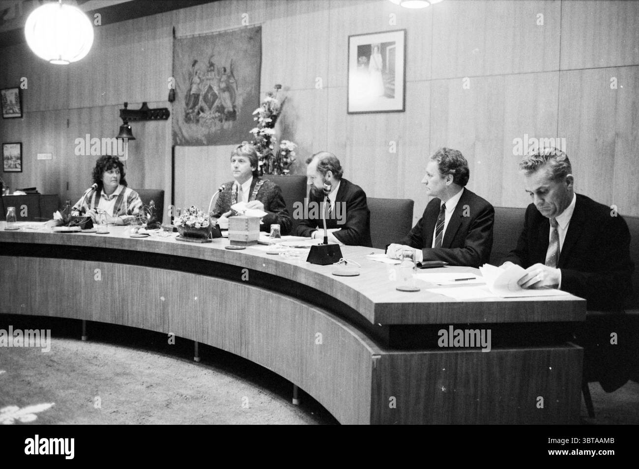 New B&W Heemskerk Heemskerk Municipal Council Heemskerk, Whizgle News, Dutch Desk, Niederlande, 1950 - 2000 am 29-04-1986. Das Bild enthält diese Themen. Die Szene zeigt eine Gruppe von fünf Personen, die in formeller Umgebung um einen großen, geschwungenen Tisch sitzen. Der Tisch ist aus Holz gefertigt, glatt poliert und hat eine moderne, leicht abgerundete Kante. Die Einzelpersonen tragen formelle Kleidung; die meisten tragen dunkle Anzüge, während eine Person ein gemustertes Outfit trägt, das einen Hauch von Kontrast verleiht. Die Menschen unterscheiden sich in Alter und Verhalten. Die Person auf der linken Seite hat mittellange, wellige Haare und Stockfoto