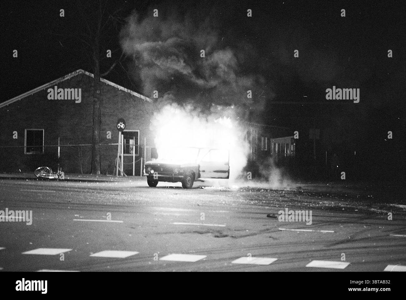 Car Wrack Fire Harmenjansbuurt Fire Brigade, Whizgle News, Dutch Desk, Niederlande, 1950 - 2000 am 01-01-1978. Das Bild enthält diese Themen. Die Szene spielt nachts mit Dunkelheit, die die Umgebung umhüllt. Im Vordergrund ist ein Fahrzeug von Flammen umgeben, das Feuer erzeugt ein intensives, flackerndes Licht, das starke Kontraste gegen die umgebenden Schatten erzeugt. Die leuchtenden Orange- und Gelbtöne der Flammen steigen dramatisch auf und erhellen den Rauch, der sich in dicken, dunklen Federn aufbläht. Das Fahrzeug selbst scheint ein Kompaktfahrzeug zu sein, dessen Merkmale durch das Feuer A verdeckt werden Stockfoto