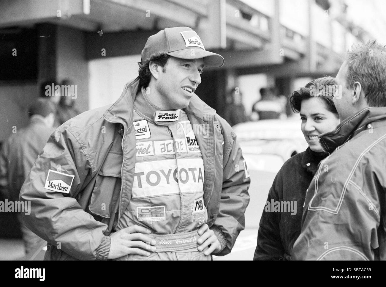 Osterrennen T. Coronel, Whizgle News, Dutch Desk, Niederlande, 1950 - 2000 am 07-04-1996. Diese Themen werden in der Abbildung angezeigt. In einem dynamischen Motorsport-Setting führt ein Trio von Einzelpersonen Gespräche und vermittelt ein Gefühl von Kameradschaft. Die Hauptfigur trägt eine markante Rennjacke mit verschiedenen Logos und trägt eine Kappe mit einem markanten Branding, was auf ihre Rolle in der Rennwelt hinweist. Seine Haltung ist entspannt, aber animiert, was darauf hindeutet, dass er eine begeisterte Geschichte teilt. Er wird von zwei anderen begleitet, einer auf jeder Seite. Links steht eine Frau mit einem leichten Lächeln Stockfoto