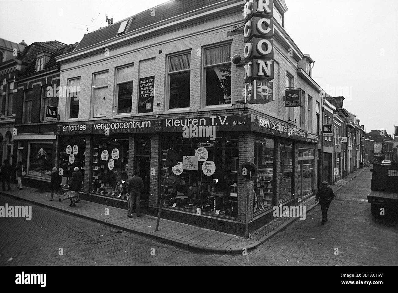 Außenansicht Marcon Außenansicht Haarlem Barrevoetestraat Niederlande, Whizgle News, Dutch Desk, Niederlande, 1950 - 2000 am 07-08-1974. Dies sind die Elemente im Bild. In der Szene steht ein zweistöckiges Gebäude an der Ecke einer belebten Straße. Die Architektur hat einen klassischen europäischen Stil mit großen Fenstern, die mit dekorativen Zierleisten verziert sind. Das Äußere ist in gedämpften Tönen gestrichen, hauptsächlich in weiß- und Grautönen, mit einigen Farbtupfern von Schildern und Displays. Im Erdgeschoss, das einem Einzelhandelsbereich gewidmet ist, wird eine Reihe von Produkten gezeigt, die durch die Expan sichtbar sind Stockfoto