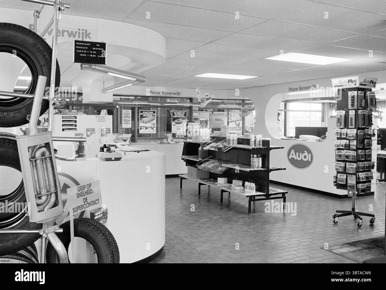 Innenraum eines Audi und Volkswagen Showrooms, Whizgle News, Dutch Desk, Niederlande, 1950 - 2000 am 11-06-1985. Dies sind die Elemente im Bild. Die Szene zeigt ein modernes Service Center mit einem übersichtlichen und übersichtlichen Layout. Der Raum ist überwiegend weiß und hell und schafft eine helle und offene Atmosphäre. Auf der linken Seite ist eine Ausstellung von Autoreifen zu sehen, in der mehrere Reifenmodelle hoch gestapelt und über einem Metallgestell hängen. In der Mitte bildet sich ein eleganter weißer Zähler, der als Hauptstation dient. Hinter dem Zähler befinden sich mehrere Wartungsbildschirme Stockfoto