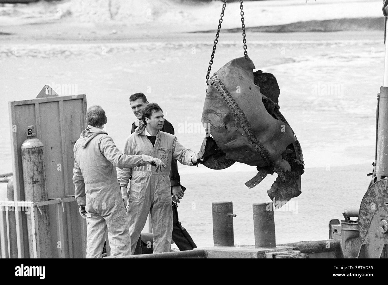 Bergungsbombe oder wahrscheinlicher eine Meeresmine aus dem Ersten Weltkrieg am Strand, Whizgle News, Dutch Desk, Niederlande, 1950 - 2000 am 02-05-1993. Diese Themen werden in der Abbildung angezeigt. Die Szene fängt einen Moment der Aktivität entlang einer Küste ein, bei dem sich drei Personen um ein großes, rostfreies Metallobjekt versammeln, das aus dem Wasser gehoben wird. Die Charaktere sind in hellen Overalls gekleidet, was auf ein Arbeitsumfeld hindeutet, und ihre Ausdrucksweisen weisen weisen auf eine Mischung aus Neugier und Ernsthaftigkeit hin. Das Metallfragment, möglicherweise ein Stück Maschine oder Wrack, hängt in der Luft und scheint düster hinein Stockfoto