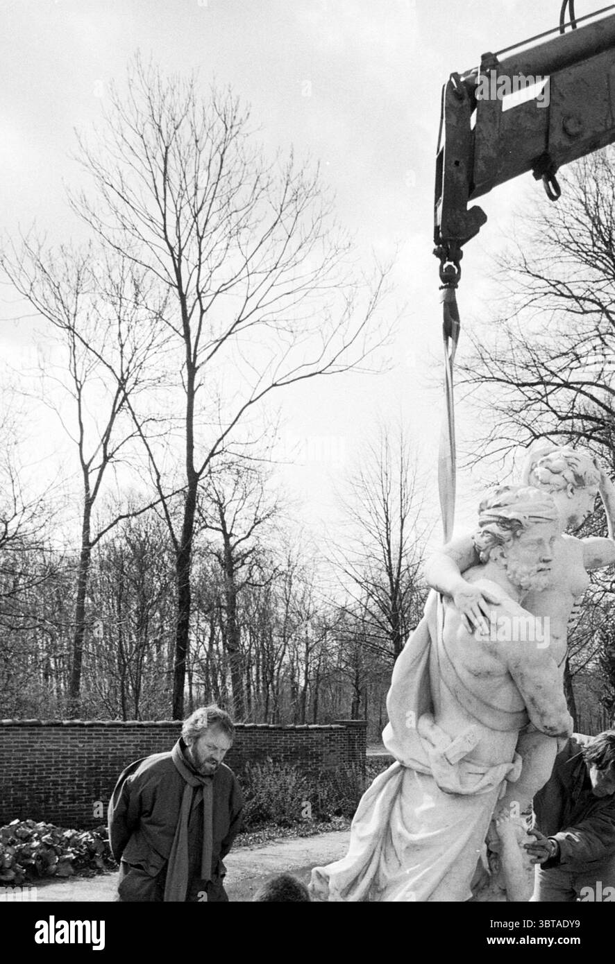 Beginnen Sie mit der Renovierung des Beeckesteyn Gartens, Whizgle News, Dutch Desk, Niederlande, 1950 - 2000 am 03-04-1992. Das Bild enthält diese Themen. In einer Szene, die von einem bewölkten Himmel geprägt ist, hebt ein Kran eine große, aufwändig geschnitzte Statue, die zwei Figuren in einer intimen Umarmung darstellt. Die Statue mit ihren detaillierten Merkmalen zeigt glatte Konturen und ausdrucksstarke Elemente, die die handwerkliche Geschicklichkeit unterstreichen. Unten beobachtet eine Gruppe von Individuen aufmerksam, ihre Ausdrucksformen sind eine Mischung aus Konzentration und Bewunderung. Die Person, die der Statue am nächsten steht, scheint ein Mann mittleren Alters zu sein Stockfoto