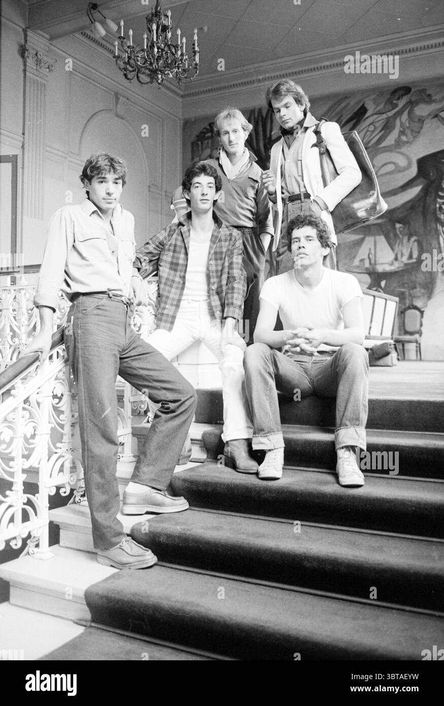 Fünf junge Männer posieren auf der Treppe in einem klassischen Interieur, Whizgle News, Dutch Desk, Niederlande, 1950 - 2000 am 09-07-1979. Die Abbildung zeigt diese Themen. In einem geräumigen, elegant eingerichteten Interieur befinden sich fünf Personen auf einer großen Treppe, die sanft geschwungen ist. Das Treppenhaus verfügt über ein klassisches schmiedeeisernes Geländer, das die kunstvolle Kulisse unterstreicht. Im Hintergrund befindet sich ein weitläufiges Wandgemälde, das der Szene ein künstlerisches Flair verleiht. Dieses Wandbild zeigt fließende Formen und abstrakte Formen, die Grau-, Schwarz- und Erdtöne vermischen, die an den Stil aus erinnern Stockfoto