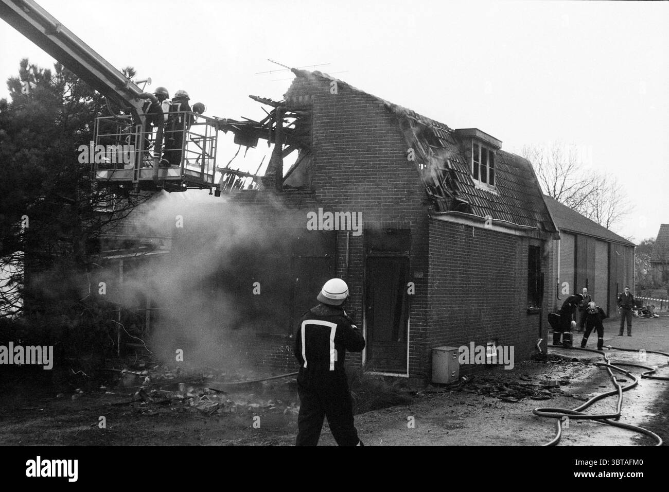 Marke Kr. Spieringweg 325 Vijfhuizen Feuerwehr Vijfhuizen Kromme Spieringweg, Whizgle News, Dutch Desk, Niederlande, 1950 - 2000 am 09-02-1990. Das Bild enthält diese Themen. Die Szene zeigt ein dramatisches Ereignis, das Feuer und Notfallmaßnahmen umfasst. Der Schwerpunkt liegt auf einem Gebäude, das erhebliche Schäden erlitten hat, was sich an den zerklüfteten Überresten des Daches und den verkohlten Abschnitten der Wände zeigt. Das Gebäude aus roten Ziegeln steht in starkem Kontrast zum dunklen Rauch, der von oben weht und eine Atmosphäre von Dringlichkeit und Spannung schafft. Links kann eine Gruppe von Feuerwehrleuten sein Stockfoto