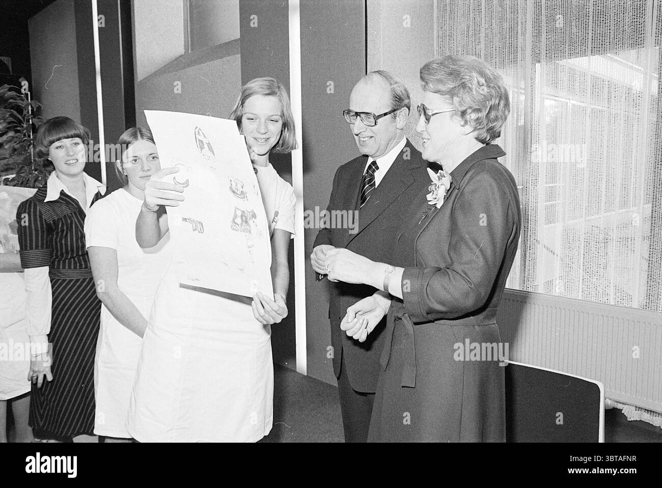 Abschiedsempfang Dr. van. Rhein Doctors Reception, Whizgle News, Dutch Desk, Niederlande, 1950 - 2000 am 10-12-1976. Dies sind die Elemente im Bild. In einem gut beleuchteten Innenbereich versammelt sich eine Gruppe von fünf Personen, die ein Gefühl von Engagement und Kameradschaft schaffen. Im Mittelpunkt steht eine junge Frau, die leicht nach vorne steht und ein großes Poster hochhält, auf dem Bilder gezeichnet sind, was darauf hinweist, dass sie etwas von Bedeutung zeigt. Ihr Ausdruck ist animiert und deutet auf Begeisterung und Stolz auf die Inhalte hin, die sie teilt. Zu ihrer Linken, ein Mann mittleren Alters, gekleidet in einem dunklen Su Stockfoto