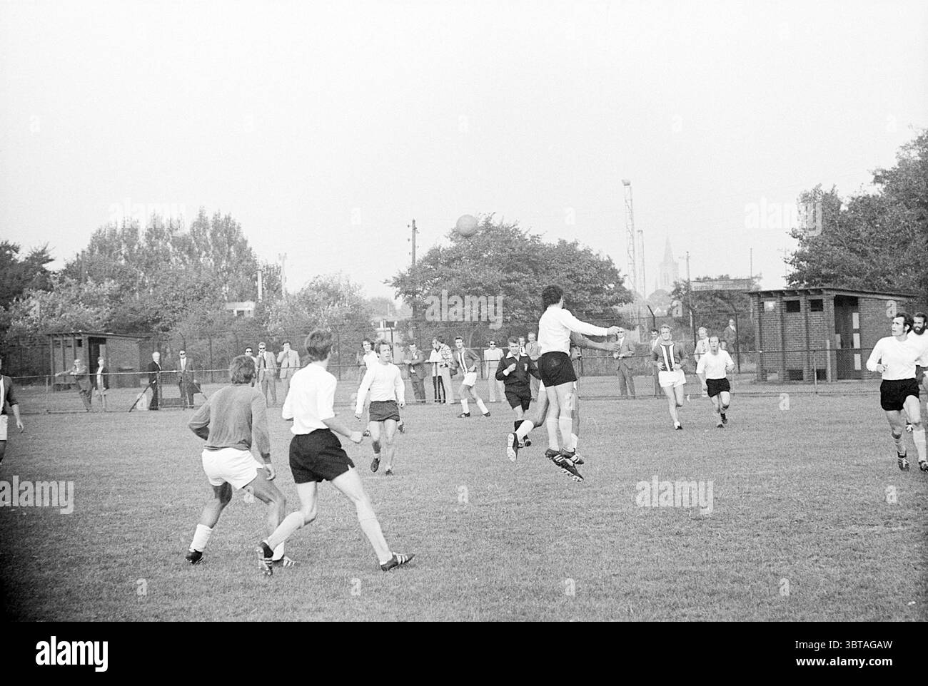 Beverwijk - H.S.V. Football, Whizgle News, Dutch Desk, Niederlande, 1950 - 2000 am 19.09.1971. Dies sind die Themen im Bild. In einem weitläufigen grünen Feld spielt eine Gruppe von Einzelpersonen ein energisches Spiel, wahrscheinlich ein Fußballspiel. Die Komposition erfasst die dynamische Bewegung und Interaktion zwischen den Spielern. Die Spieler tragen eine Mischung aus hellen und dunklen Shorts, wobei einige verschiedene Trikots tragen, die in Stil und Farbe variieren. Ein Spieler, der hoch in der Luft ist, greift zum Ballanführer und veranschaulicht die Sportlichkeit und Intensität des Spiels. Um die zentrale Szene herum o Stockfoto Beverwijk - H.S.V. Football, Whizgle News, Dutch Desk, Niederlande, 1950 - 2000 am 19.09.1971. Dies sind die Themen im Bild. In einem weitläufigen grünen Feld spielt eine Gruppe von Einzelpersonen ein energisches Spiel, wahrscheinlich ein Fußballspiel. Die Komposition erfasst die dynamische Bewegung und Interaktion zwischen den Spielern. Die Spieler tragen eine Mischung aus hellen und dunklen Shorts, wobei einige verschiedene Trikots tragen, die in Stil und Farbe variieren. Ein Spieler, der hoch in der Luft ist, greift zum Ballanführer und veranschaulicht die Sportlichkeit und Intensität des Spiels. Um die zentrale Szene herum o Stockfoto