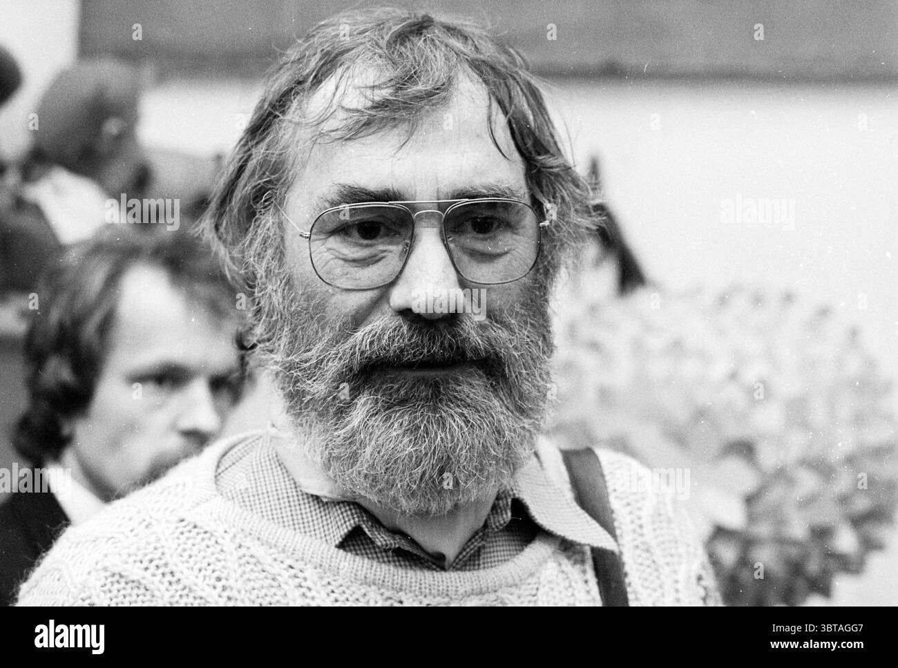 Doll Talk House Fabeltjeskrant Leen Valkenier, Whizgle News, Dutch Desk, Niederlande, 1950 - 2000 am 02-02-1979. Dies sind die Themen im Bild. In der Szene steht ein Mann mit vollem, grauen Bart und dicker Brille im Vordergrund. Sein Ausdruck ist kontemplativ und verströmt einen Hauch von Erfahrung und Weisheit. Er trägt einen lockeren Strickpullover, der seinem Aussehen einen gemütlichen, informellen Touch verleiht. Der Hintergrund zeigt verschwommene Zahlen, die auf eine Versammlung oder ein Ereignis hinweisen, was zu einem Gefühl der Gemeinschaft oder Interaktion beiträgt. Die Farben sind überwiegend gedämpft, mit Grautönen, W Stockfoto