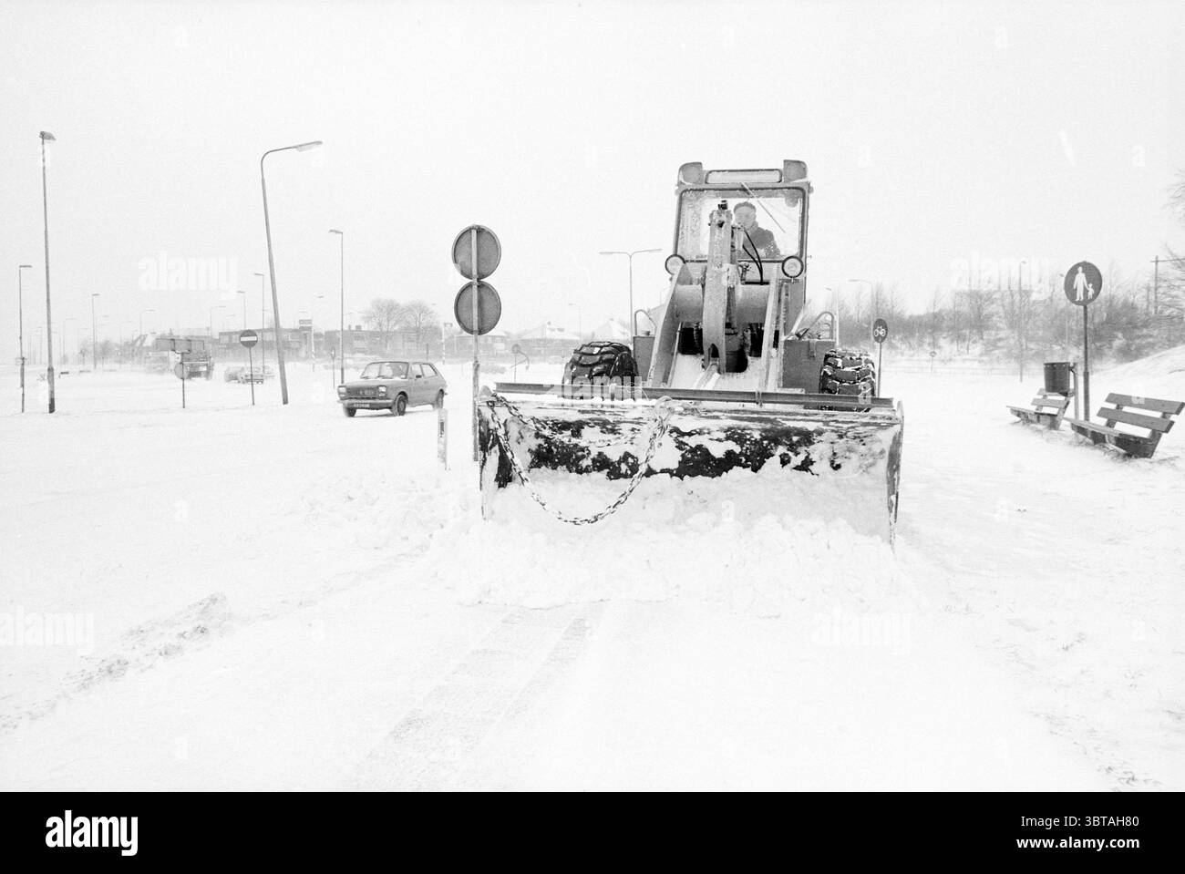 Schneepflug in IJm. Snow IJmuiden the Netherlands, Whizgle News, Dutch Desk, Niederlande, 1950 - 2000 am 13-02-1979. Dies sind die Themen im Bild. Die Szene fängt eine Winterlandschaft ein, die aufgrund des starken Schneefalls überwiegend in unterschiedlichen weiß- und Grautönen gemalt ist. Im Vordergrund dominiert ein großer Schneepflug die Komposition, dessen Klinge mit einer dicken Schneeschicht bedeckt ist, die zur Seite geschoben wurde, während das Fahrzeug selbst mit seinen gedämpften Farben etwas robust und industriell wirkt. Rund um den Schneepflug ist der Boden stark mit Neuschnee bedeckt und bietet ein glattes, unberührtes Qu Stockfoto
