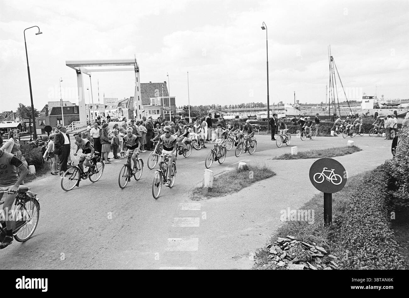 Muggenronde 1963 Muggenronde, Whizgle News, Dutch Desk, Niederlande, 1950 - 2000 am 22-07-1963. Dies sind die Themen im Bild. Die Szene zeigt ein lebhaftes Outdoor-Event rund um eine Radtour. Eine Gruppe von Radfahrern, die in passenden Trikots gekleidet sind, wird bei der Navigation auf einem gekrümmten Weg besonders hervorgehoben. Die Radfahrer zeigen eine Reihe von Haltungen, von denen einige energetisch wirken, während andere entspannter sind. Am Rande des Weges steht eine Menge Zuschauer, von denen viele jubeln und klatschen, sichtbar begeistert von der Atmosphäre. Einige Personen halten fest Stockfoto