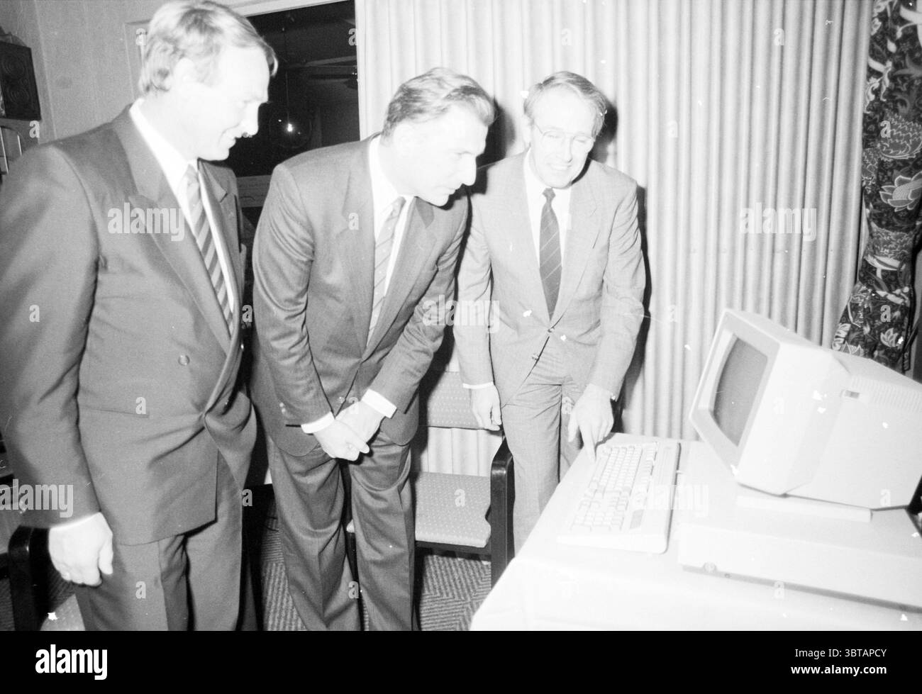 Inbetriebnahme beschädigter Geräte DGSM Inbetriebnahme der Lotsenpilotage IJmuiden the Netherlands, Whizgle News, Dutch Desk, Niederlande, 1950 - 2000 am 27-11-1989. Dies sind die Themen im Bild. Drei Männer versammeln sich um einen Desktop-Computer, deren Ausdruck ein Gefühl der Neugier und Intrige widerspiegelt. Sie sind in formeller Kleidung gekleidet, mit dunklen Anzügen und Krawatten, was auf einen wichtigen oder beruflichen Anlass hindeutet. Der Mann in der Mitte neigt sich leicht nach vorne, sein Gesicht leuchtet mit einer Mischung aus Konzentration und Spannung, während er genau auf den Bildschirm schaut. Auf seine le Stockfoto