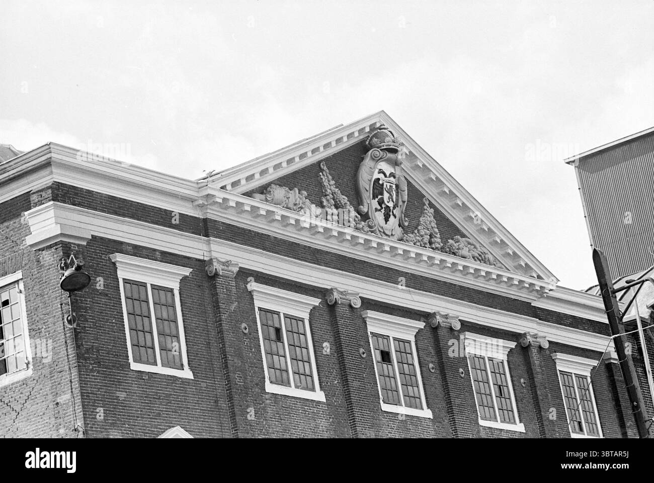 Wappen der Zuckerfabrik Wappen der Familie, Whizgle News, Dutch Desk, Niederlande, 1950 - 2000 am 24-09-1968. Dies sind die Elemente im Bild. Die Szene zeigt eine architektonische Fassade eines historischen Gebäudes, die durch eine reiche, strukturierte Backsteinoberfläche gekennzeichnet ist. Die Struktur ist mit komplizierten Elementen geschmückt, die die Aufmerksamkeit nach oben lenken, insbesondere auf das verzierte Wappen am Gipfel, das mit floralen Motiven und einem zentralen Emblem verziert ist, das wahrscheinlich historische Bedeutung symbolisiert. Die Farbpalette wird von Erdtönen dominiert, vor allem von tiefem Rot- und Braunton Stockfoto