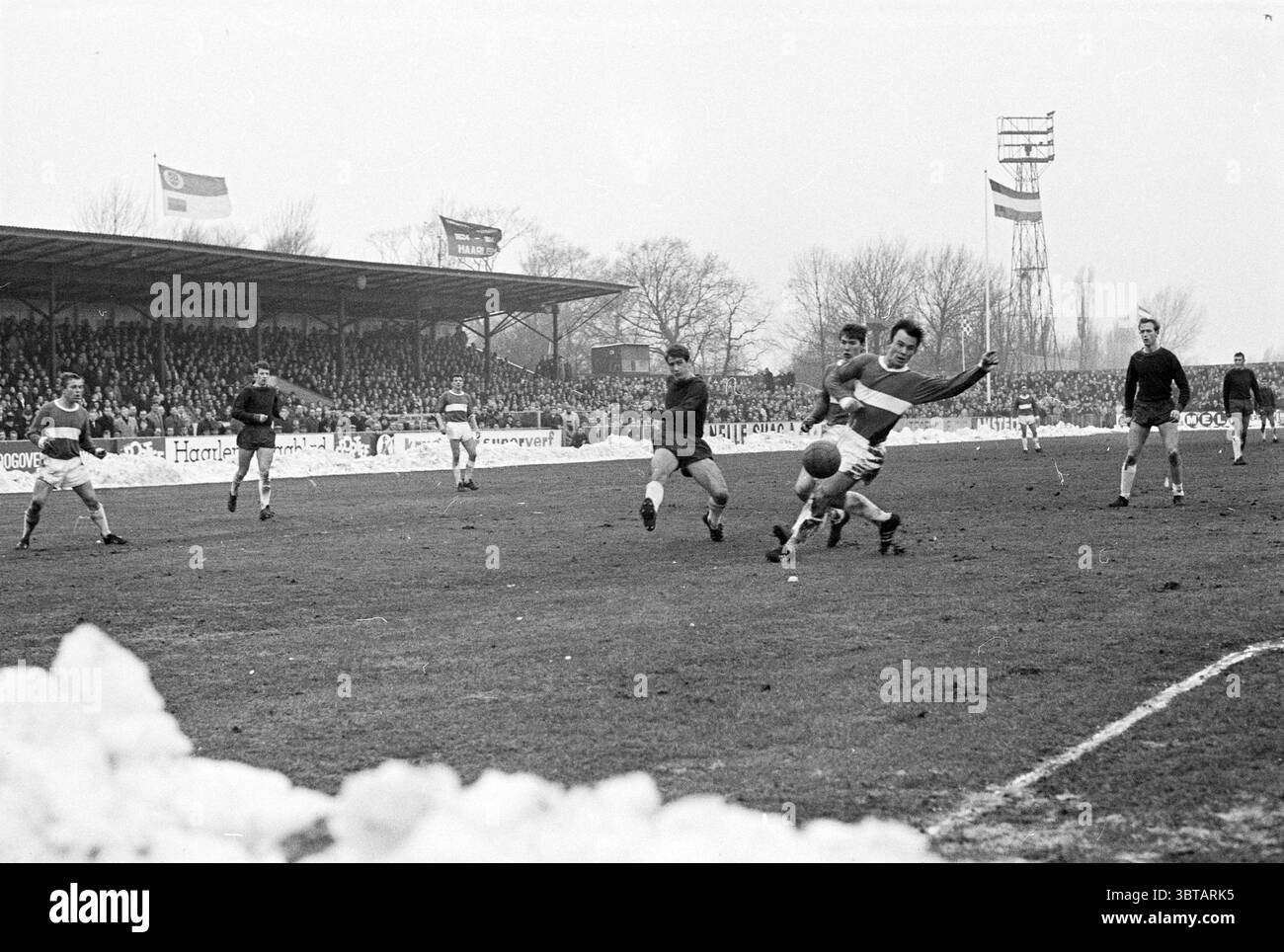 Haarlem - Holland Sports Football Haarlem, Whizgle News, Dutch Desk, Niederlande, 1950 - 2000 am 04-02-1968. Diese Themen werden in der Abbildung angezeigt. Die Szene zeigt ein lebhaftes Fußballspiel, das an einem monochromen Wintertag stattfindet und zu einer nostalgischen Atmosphäre beiträgt. Das Spielfeld ist mit deutlichen Grasflecken gekennzeichnet, einige Bereiche, die von Schneeresten verdeckt sind, was auf die jüngsten Wetterbedingungen hinweist. Im Vordergrund fängt ein dynamischer Moment einen Spieler in der Mitte der Action ein, während er versucht, den Ball zu kicken, während er von einem Gegner herausgefordert wird. Die Spannung zwischen den beiden Spielern ist spürbar, wie sie sind Stockfoto
