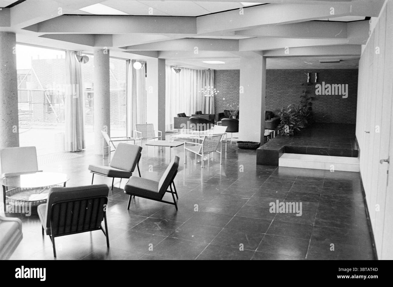 Innenraum eines Zimmers mit verschiedenen Sitzbereichen in einem Krankenhaus., Whizgle News, Dutch Desk, Niederlande, 1950 - 2000. Diese Themen werden in der Abbildung angezeigt. Die Szene präsentiert ein geräumiges, modernes Interieur, das sich durch ein schlankes Design und ein offenes Layout auszeichnet. Der Boden besteht aus großen, dunklen quadratischen Fliesen, die einen starken Kontrast zu den helleren Farben der Wände und Möbel bieten. Im Vordergrund sind mehrere minimalistische Stühle mit einer Kombination aus Metall- und Stoffelementen lässig angeordnet. Die kantigen Linien und der zeitgenössische Stil vermitteln ein Gefühl von Komfort während des Hauptbetriebs Stockfoto