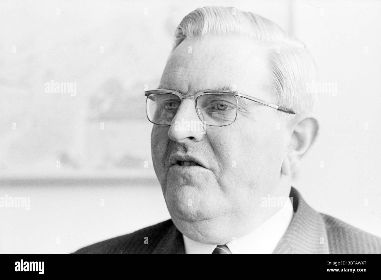 Alderman Gerritsen Aldermen, Whizgle News, Dutch Desk, Niederlande, 1950 - 2000 am 16-04-1970. Dies sind die Themen im Bild. Die visuelle Szene zeigt einen Mann mittleren Alters mit einem komponierten Ausdruck, der für sein ordentlich gestyltes, helles Haar bekannt ist, das zurückgeschliffen ist. Er trägt eine rechteckige Brille, die einen intellektuellen Touch verleiht, und seine Gesichtszüge sind etwas prall, was auf ein freundliches Verhalten hindeutet. Seine Kleidung besteht aus einem dunklen Anzug, der sich vom helleren Hintergrund abhebt und ihm ein formelles Aussehen verleiht. Die subtile Textur des Anzugs wird vorgeschlagen, möglicherweise weist dies auf einen hin Stockfoto
