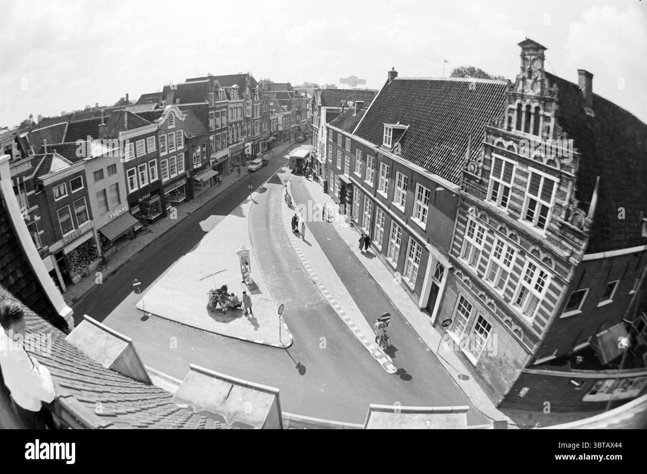 Bushaltestelle in der lange Houtstraat Haarlem lange Houtstraat Nederland., Whizgle News, Dutch Desk, Niederlande, 1950 - 2000. Diese Themen sind in der Abbildung dargestellt. Die Szene bietet einen Blick aus der Vogelperspektive auf eine malerische Straße, gesäumt von charmanten, historischen Gebäuden. Die architektonischen Stile variieren, wobei einige Gebäude mit komplizierten Giebeln und Fassaden mit dekorativen Elementen versehen sind. Die Dächer sind mit einer Mischung aus dunklen Fliesen und helleren Materialien versehen, die einen auffälligen Kontrast schaffen. Die Straße biegt sich sanft und führt das Auge in die Ferne. Mehrere Fußgänger können gemächlich spazieren gehen und eine se hinzufügen Stockfoto