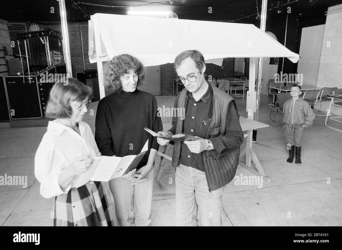 Übergabe des Marktstandes an Amnesty International Hillegom Übergabe und Übertragung von Hillegom, Whizgle News, Dutch Desk, Niederlande, 1950 - 2000 am 01-07-1988. Dies sind die Themen im Bild. In einem geräumigen, schwach beleuchteten Innenraum stehen drei Personen eng zusammen und führen Gespräche. Der Raum verfügt über eine weitläufige Kulisse aus dunklen Wänden, mit etwas Licht, das von glänzenden Oberflächen abprallt und ein etwas reflektierendes Ambiente schafft. Im Hintergrund deuten Blicke auf gespeicherte Objekte auf einen kreativen Raum hin, möglicherweise ein Gemeindezentrum oder eine künstlerische Werkstatt. Links, eine Frau W Stockfoto