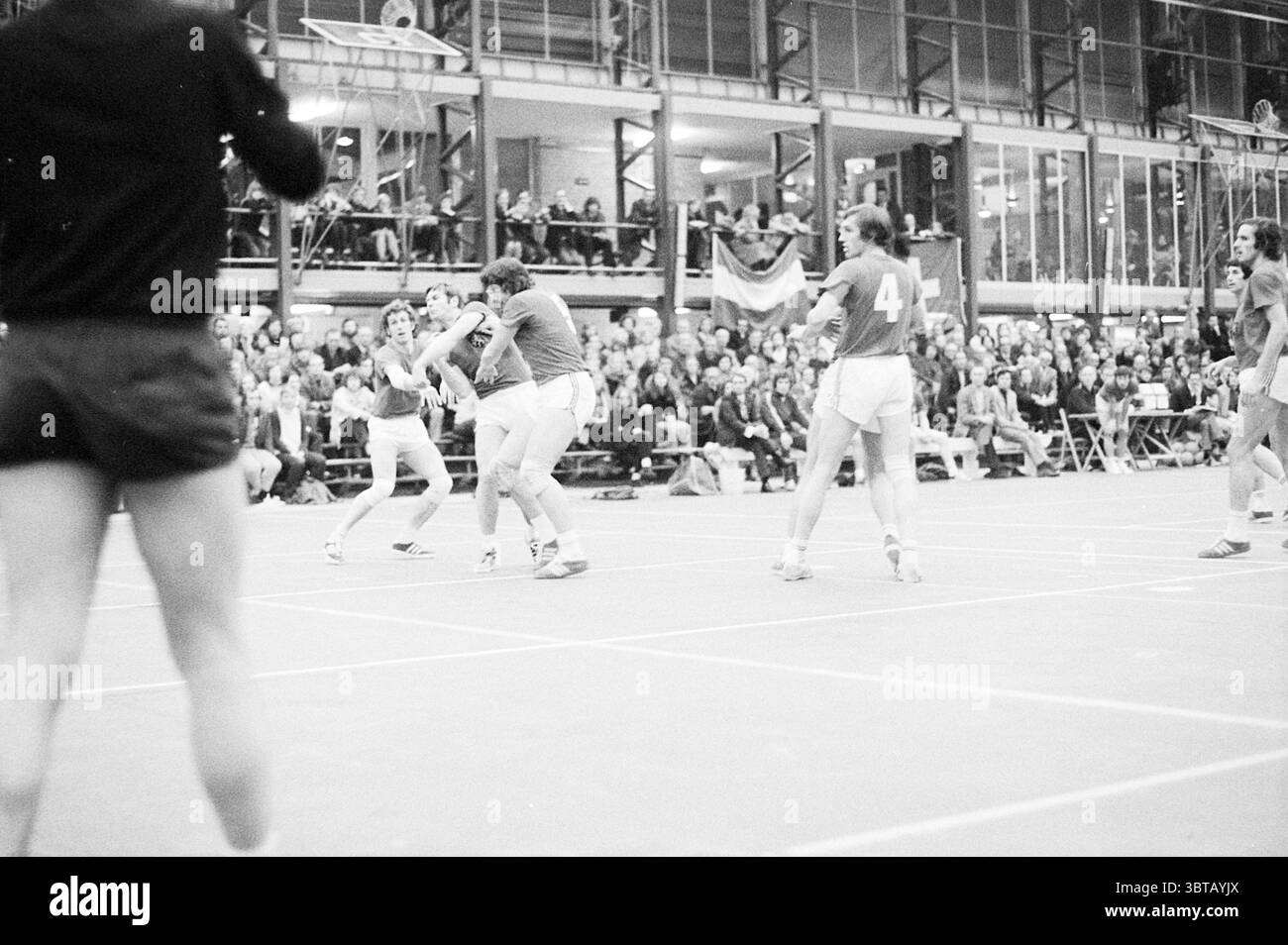 Handball Niederlande - Schweiz Handball, Whizgle News, Dutch Desk, Niederlande, 1950 - 2000 am 05-02-1972. Dies sind die Elemente im Bild. Die Szene spielt in einer großen Sporthalle, die vor Energie und Spannung strotzt. Der Boden ist mit deutlichen Linien markiert, die verschiedene Höfe abgrenzen, die alle aus unzähligen Spielen gut abgenutzt sind. Im Vordergrund steht eine Gruppe von Athleten, die intensiv an einem Wettkampf beteiligt sind. Sie sind in passenden Uniformen gekleidet, hauptsächlich in Blau- und Weißtönen, die sich von den neutralen Tönen der Arena abheben. Die Spieler zeigen eine Variette Stockfoto