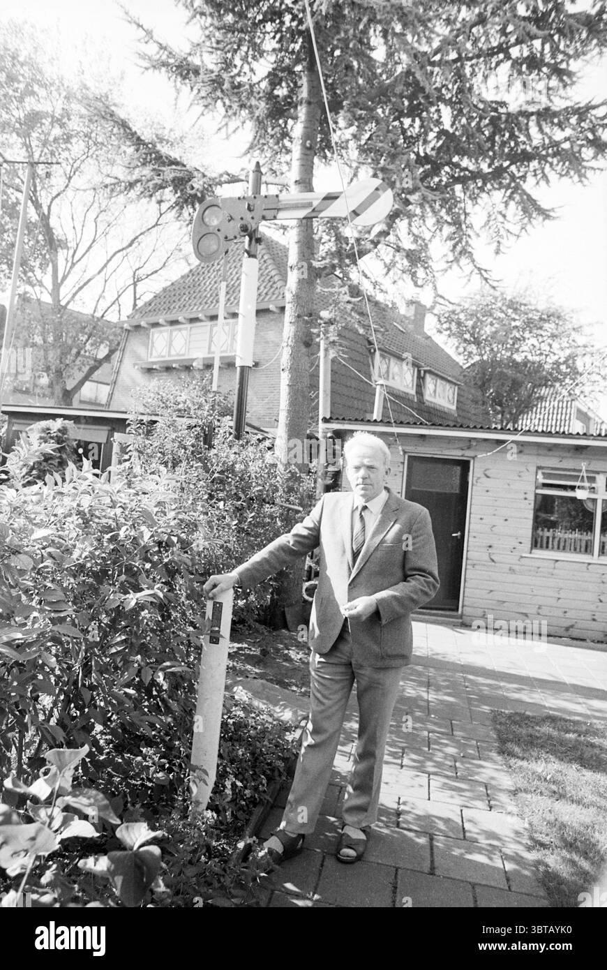 Herr Plijter + Semaphore im Garten Santpoort, Whizgle News, Dutch Desk, Niederlande, 1950 - 2000 am 11. 10. 1990. Die Abbildung zeigt diese Themen. In dieser Szene steht ein älterer Mann selbstbewusst neben einem Signalpfeiler, der mit einem Signalarm verziert ist. Er trägt einen formellen grauen Anzug, kombiniert mit einem hellen Hemd und dunklen Schuhen, was ihm ein würdevolles Aussehen verleiht. Sein weißes Haar steht im Kontrast zu seiner Kleidung, und er schaut nachdenklich zur Seite, was darauf hindeutet, dass er tief in Nachdenken steckt oder an die Vergangenheit erinnert. Um ihn herum blüht Grün, mit Büschen und Ornamenten Stockfoto