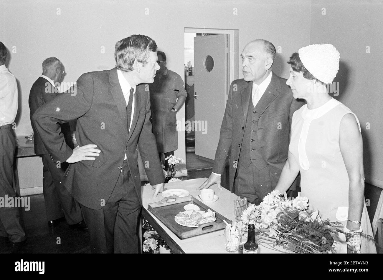HR. Jubiläum und Empfang Kalf Haarlems Dagblad etc. Und IJmuider Courant and Koeri, Whizgle News, Dutch Desk, Niederlande, 1950 - 2000 am 15.09.1970. Dies sind die Themen im Bild. In einem gut beleuchteten Innenraum führt eine kleine Gruppe von Personen ein animiertes Gespräch. Die Szene zeichnet sich durch eine Ästhetik aus der Mitte des Jahrhunderts mit einer neutralen Wand aus, die die Menschen und Objekte im Raum betont. Im Vordergrund neigt sich ein Mann in dunklem Anzug und Krawatte leicht nach vorne, wobei seine Körpersprache Interesse oder vielleicht Besorgnis zum Ausdruck bringt. Sein Haar ist ordentlich Stockfoto