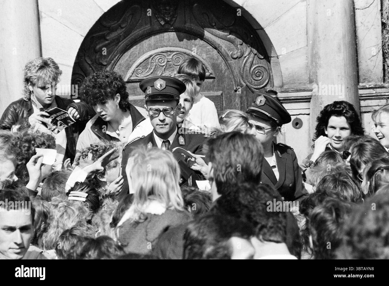 Performance von Theo und Thea Frans Hals Museum Performance Haarlem the Netherlands, Whizgle News, Dutch Desk, Niederlande, 1950 - 2000 am 12-04-1986. Dies sind die Elemente im Bild. Die Szene ist voller Aktivität, mit einer überfüllten Umgebung im Freien, wahrscheinlich vor einem imposanten Gebäude mit einem detaillierten Eingang. Die Architektur zeigt kunstvolle Schnitzereien, die auf historische Bedeutung hinweisen. Im Vordergrund ist eine dichte Ansammlung von Menschen eng zusammengepackt, überwiegend junge Menschen, die begeistert und eifrig zu sein scheinen. Die Menge ist animiert, mit vielen Gesichtern, die sich zuwenden Stockfoto