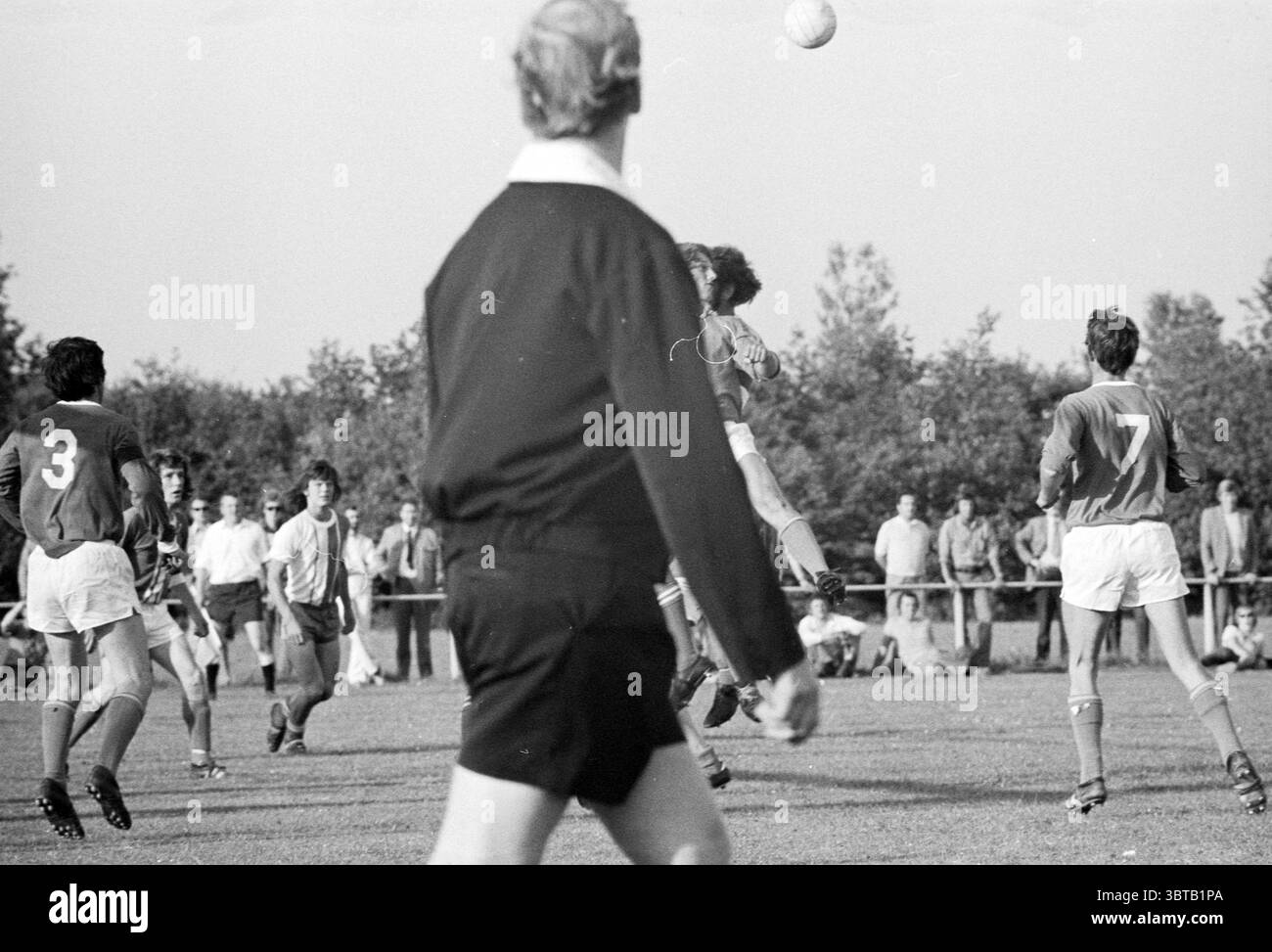 ADO '20 - Hoofddorp Football, Whizgle News, Dutch Desk, Niederlande, 1950 - 2000 am 11-06-1973. Dies sind die Elemente im Bild. Die Szene fängt einen lebendigen Moment auf einem Sportplatz ein, voller Energie und Vorfreude. Im Vordergrund steht ein Schiedsrichter, der eine schwarze Kleidung trägt, die einen scharfen Kontrast zu den helleren Farben der Spieler um ihn herum bildet. Sein Rücken wird dem Betrachter zugewandt und zeigt eine ordentlich gekämmte Frisur und eine Haltung, die Aufmerksamkeit auf die sich entfaltende Handlung suggeriert. Im Hintergrund sind mehrere Spieler in einem Wettkampfmoment beteiligt. Der Athleten Stockfoto
