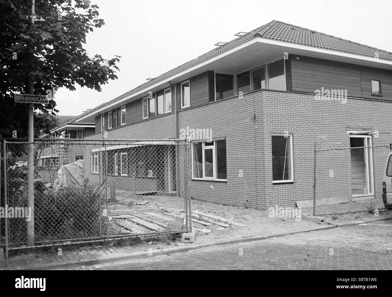Neubau von Ramplaan Haarlem Haarlem Ramplaan Niederlande, Whizgle News, Dutch Desk, Niederlande, 1950 - 2000 am 06-09-1994. Das Bild enthält diese Themen. Die Szene fängt eine Wohnbaustelle ein, die durch einen modernen architektonischen Stil geprägt ist. Im Vordergrund befinden sich zwei neu gebaute zweistöckige Gebäude, deren Äußere mit einer Kombination aus rötlichen Ziegeln und dunklen Holzpaneelen verkleidet ist, was einen auffälligen Kontrast bietet. Das Dach ist flach, mit einem leichten Überhang, was dem Gebäude ein zeitgenössisches Gefühl verleiht. Um die Gebäude herum befindet sich ein Maschendrahtzaun, etwas r Stockfoto