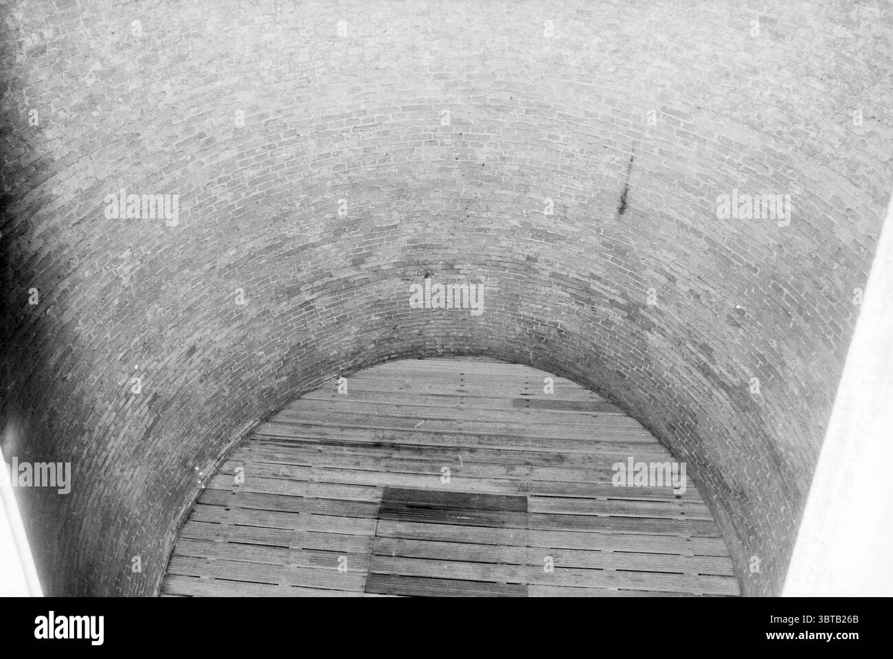 Int. Eiskeller [auf dem Estate] Waterland. Eislaufbahn Eishockey Velsen-Zuid Rijksweg, Whizgle News, Dutch Desk, Niederlande, 1950 - 2000 am 02-06-1989. Das Bild enthält diese Themen. Die Szene zeigt einen tiefen, kreisförmigen Brunnen mit glatten, geschwungenen Ziegelwänden, die hoch über die Perspektive des Betrachters ragen. Die Ziegel sind verwittert und zeigen eine Mischung aus dunkelgrauen und helleren Tönen, die auf das Alter und die dauerhafte Präsenz der Struktur hinweisen. Am Boden des Brunnens befindet sich eine hölzerne Plattform aus rauen, unpolierten Dielen, die horizontal liegen. Das Holz mit seiner natürlichen Körnung ist glatt Stockfoto