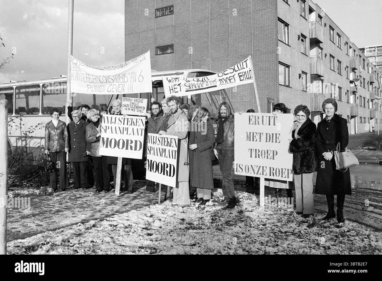 Spanplatten-Demonstratoren bei Bus-Demonstration, Whizgle News, Dutch Desk, Niederlande, 1950 - 2000 am 28-11-1978. Diese Themen sind in der Abbildung dargestellt. In der Szene steht eine Gruppe von Einzelpersonen vor einem mehrstöckigen Wohngebäude, das sich durch ein einfaches, funktionales Design auszeichnet. Die Architektur besteht aus einer Mischung aus Ziegel und Beton, mit einer Reihe von Fenstern, die ein rhythmisches Muster über die Fassade schaffen. Die Menschen sind in einer Reihe angeordnet und zeigen eine Vielzahl von Ausdrücken, von ernsthaft bis kontemplativ, da sie große Banner und Schilder halten. Ihre Kleidung repräsentiert eine Mischung aus styl Stockfoto