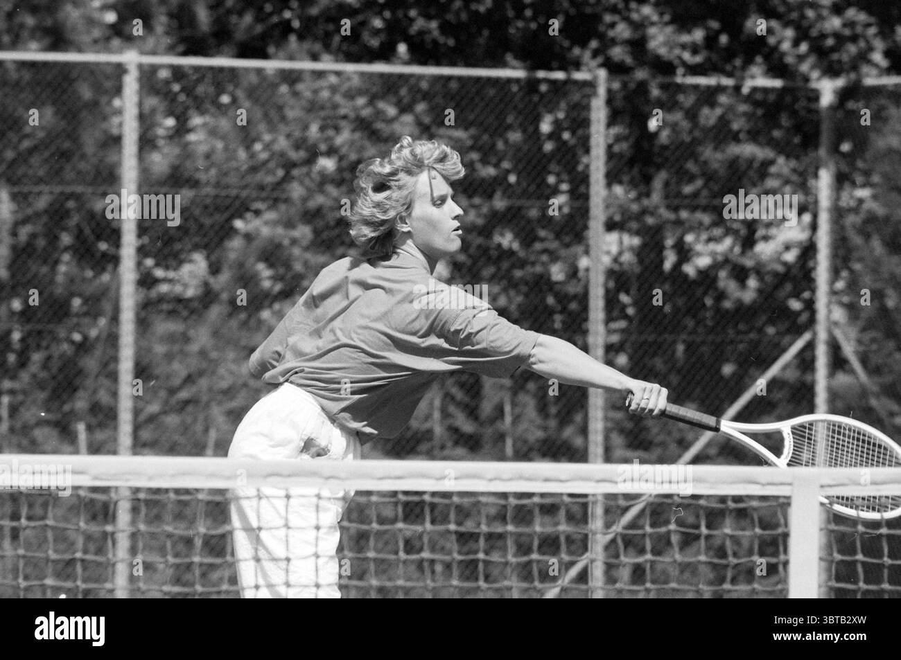 Tennisspielerin Sonja Drau Lisse, Whizgle News, Dutch Desk, Niederlande, 1950 - 2000 am 28-05-1990. Dies sind die Themen im Bild. Die Szene fängt einen dynamischen Moment auf einem Tennisplatz ein, umgeben von einer üppigen grünen Umgebung. Eine Spielerin befindet sich mitten im Schwung, ihr Körper ist abgewinkelt, während sie sich intensiv auf den eintretenden Ball konzentriert. Ihr Antrag schlägt sowohl Entschlossenheit als auch Anmut vor. Sie trägt ein helles, langärmeliges Oberteil, kombiniert mit einer weißen Hose, die leicht fließt, während sie sich bewegt und ein Gefühl von Fließfähigkeit schafft. Ihr Haar ist in weichen Locken gestylt, die von der Brise subtil zerzaust werden und ihr Energie verleihen Stockfoto