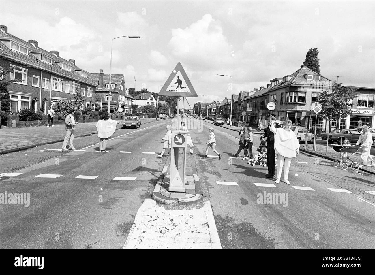 Verkehrsbrigade Rijksstraatweg Verkehrssicherheit Haarlem Rijksstraatweg Niederlande, Whizgle News, Dutch Desk, Niederlande, 1950 - 2000 am 26-08-1985. Die Abbildung zeigt diese Themen. Die Szene fängt eine ruhige Straße ein, flankiert von Wohngebäuden mit unterschiedlichen architektonischen Stilen, die ein Gefühl für eine Vorstadtgegend vermitteln. Die Strukturen zeigen eine Mischung aus hellen und dunklen Ziegeltönen, und einige verfügen über Giebeldächer, die der Umgebung Charakter verleihen. Im Vordergrund ist an der Straße ein Straßenübergang deutlich abgegrenzt, der bis auf wenige Fußgänger meist leer ist. Der Querweg ist markiert mit Stockfoto