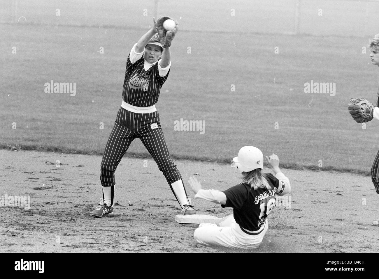 Softball: Terrasvogels - Twins, Whizgle News, Dutch Desk, Niederlande, 1950 - 2000 am 19.08.1990. Diese Themen sind in der Abbildung dargestellt. Die Szene fängt einen dynamischen Moment auf einem Softballfeld ein, in dem zwei Spieler ein intensives Spiel führen. Der Athlet auf der linken Seite ist zielgerichtet und trägt eine auffällige gestreifte Uniform mit dunklen und hellen Linien. Sie befindet sich in einer fesselnden Haltung, die Arme sind nach oben gestreckt, während sie sich auf einen Ball vorbereitet. Ihr Ausdruck vermittelt Entschlossenheit und Konzentration, betont durch ein Visier, das ihre Augen vor der Sonne schützt. In der Zwischenzeit, rechts, ein Spieler sl Stockfoto