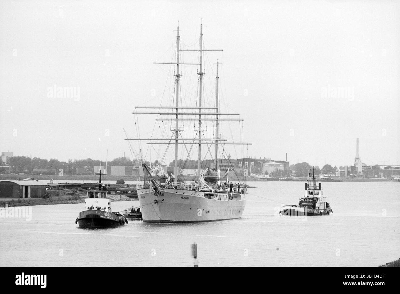 Abschleppen der Pollux nach Amsterdam, Whizgle News, Dutch Desk, Niederlande, 1950 - 2000 am 16.06.1991. Die Abbildung zeigt diese Themen. In der Szene steht ein majestätisches Großschiff im Mittelpunkt, dessen drei hoch aufragende Masten nach oben ragen und mit aufwändig getakteten Segeln verziert sind, die sanft im Wind wehen. Das Schiff ist in einem sanften Grau gemalt und verschmilzt subtil mit dem bewölkten Himmel, der ein gedämpftes Licht über das Wasser wirft. Um das Schiff herum spiegelt das ruhige Wasser die gedämpften Töne des Schiffes und die bewölkte Atmosphäre wider und schafft ein Gefühl der Harmonie. Ein kleinerer Schlepper bewegt sich entlang des t Stockfoto