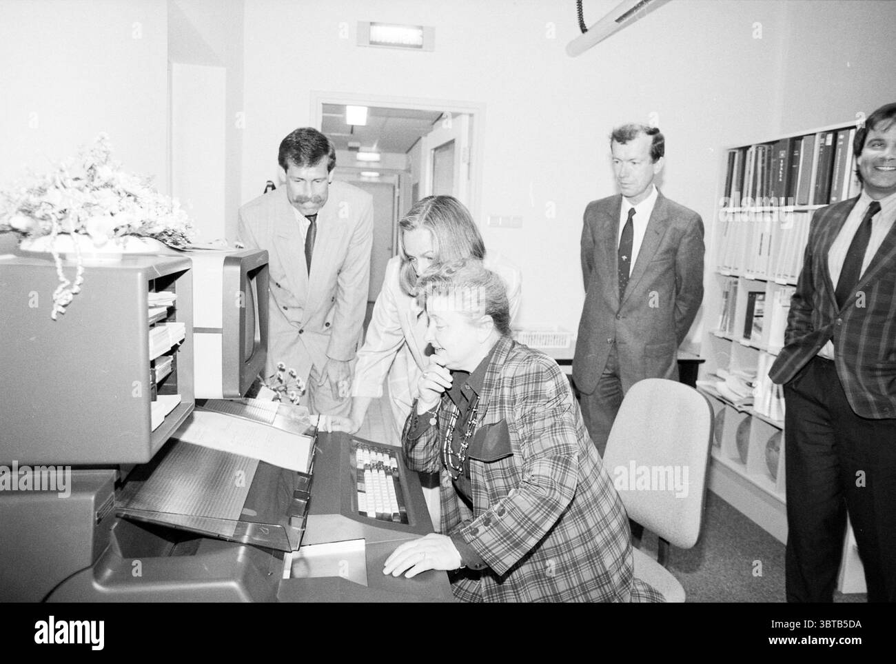 Eröffnung der Station Haarlem Eröffnung der Öffnungen Inbetriebnahme Station Haarlem Niederlande, Whizgle News, Dutch Desk, Niederlande, 1950 - 2000 am 11-05-1989. Diese Themen sind in der Abbildung dargestellt. In einer monochromatischen Umgebung versammelt sich eine Gruppe von Individuen um ein Retro-Computerterminal, das auf den Bildschirm fokussiert ist. Zwei Personen, eine in einem gemusterten Blazer und eine andere in einem formelleren Anzug, lehnen sich eng an, ihre Ausdrucksformen sind eine Mischung aus Neugier und Konzentration. Die Person in dem gemusterten Blazer scheint in der Bedienung zu sein, möglicherweise tippen oder die Steuerelemente des Computers verwenden. Hinter dem Stockfoto