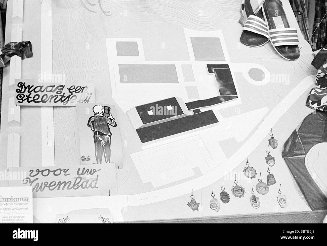 Model Swimming Pool Zandvoort Model, Whizgle News, Dutch Desk, Niederlande, 1950 - 2000 am 11-04-1973. Diese Themen sind in der Abbildung dargestellt. In der Szene zeigt eine flache Fläche eine große, detaillierte Karte an, die durch verschiedene Formen gekennzeichnet ist, die Gebäude, Wege und Zonenbereiche darstellen. Die Grundfarbe der Karte ist ein gedämpfter neutraler Ton, wodurch die komplizierten Linien und Abschnitte deutlich hervorstechen. Mehrere Elemente werden strategisch um die Karte herum platziert. Auf der einen Seite gibt es zwei Paar Schuhe; eine ist eine legere Sandale und die andere scheint ein formellerer Slip-On zu sein, beides trägt zu einem Hauch bei Stockfoto
