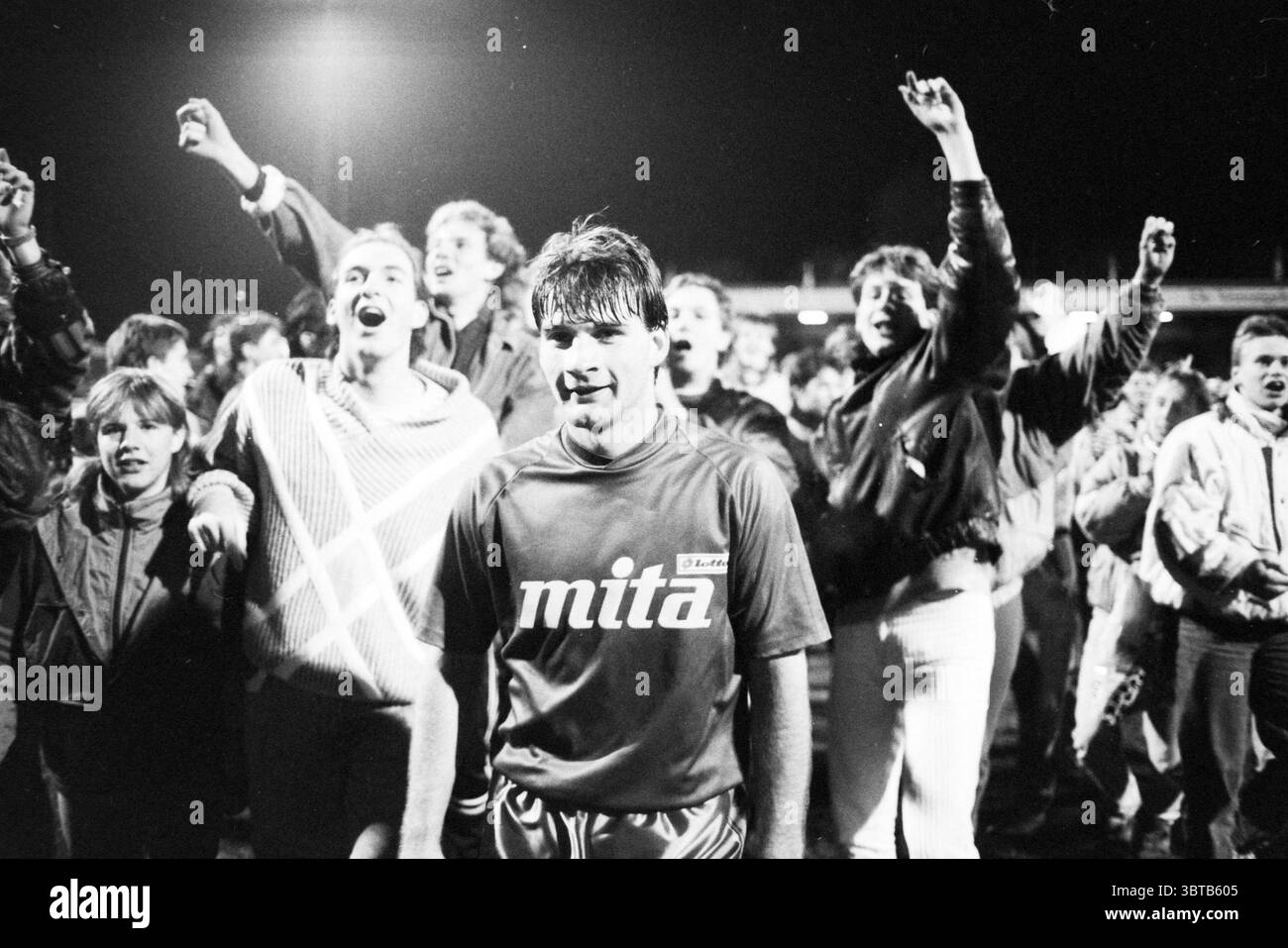 Haarlem - PSV Football Haarlem, Whizgle News, Dutch Desk, Niederlande, 1950 - 2000 am 02-11-1988. Dies sind die Elemente im Bild. Die Szene fängt einen lebendigen Moment voller Emotionen und Energie ein. Im Vordergrund steht ein junger Athlet mit einem Sportrikot, auf dem ein Markenlogo auf der Brust sichtbar ist. Sein Ausdruck ist eine Mischung aus Erleichterung und Freude, ein subtiles Lächeln, das auf seinen Lippen spielt, während er den Triumph des Augenblicks verkörpert. Hinter ihm füllt ein Meer jubelnder Fans den Hintergrund, ihre Gesichter leuchten vor Aufregung und Überschwänglichkeit. Viele heben ihre Arme, Fäuste klappern Stockfoto