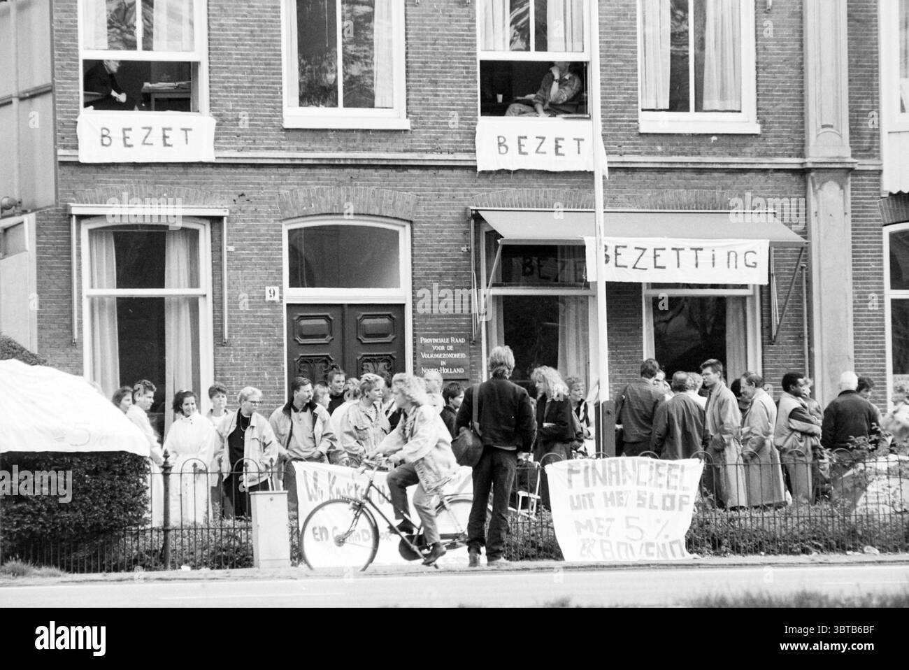 Besetzung des Provinzrates des öffentlichen Gesundheitsamtes durch Kampagne Krankenschwestern Haarlem Niederlande, Whizgle News, Dutch Desk, Niederlande, 1950 - 2000 am 11-05-1989. Diese Themen werden in der Abbildung angezeigt. Die Szene zeigt eine Versammlung zahlreicher Individuen vor einem Backsteingebäude, das durch große Fenster gekennzeichnet ist. Die Fassade vermittelt ein Gemeinschaftsgefühl, wobei einige Leute auf dem Bürgersteig stehen und andere aus den oberen Fenstern blicken. Die Menge besteht hauptsächlich aus Erwachsenen, mit ein paar Fahrrädern und Gegenständen, die verstreut sind, was zu einer ungezwungenen und doch organisierten Atmosphäre beiträgt. Wichtig Stockfoto