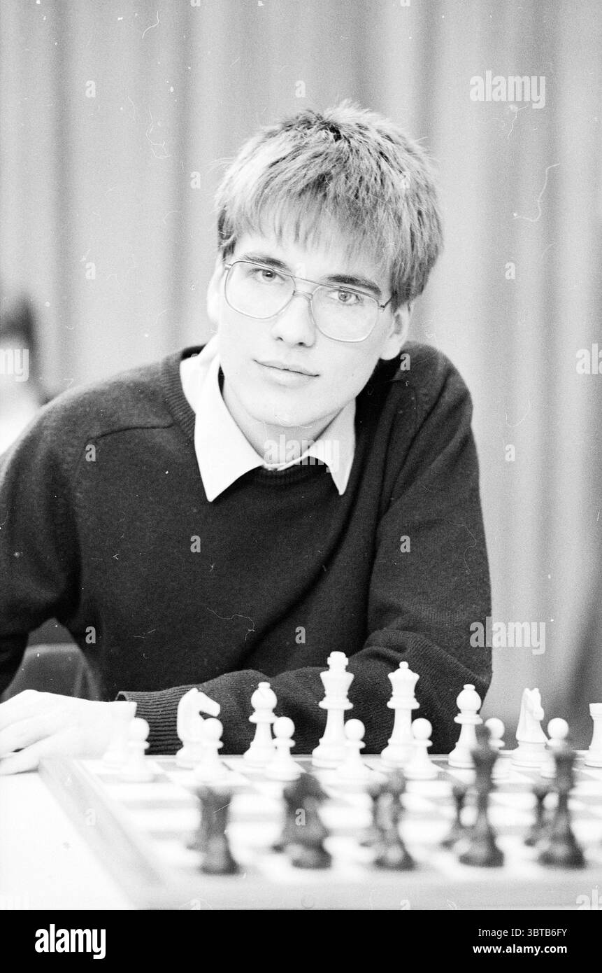 Porträts der Großmeistergruppe H.S.T. Blast Furnace Chess Tournament Wijk aan Zee, Whizgle News, Dutch Desk, Niederlande, 1950 - 2000 am 17.01.1986. Das Bild enthält diese Themen. Die Szene zeigt einen jungen Menschen, der auf einem Spielbrett sitzt. Ihr Gesicht hat einen kontemplativen Ausdruck, der auf eine tiefe Konzentration und Strategie bei der Vorbereitung auf den nächsten Schritt hindeutet. Die junge Person hat hellbraune, leicht zerzauste Haare und trägt eine große, runde Brille, die ihr nachdenkliches Verhalten unterstreicht. Das Schachbrett davor zeigt eine organisierte Anordnung von Stücken: Stockfoto
