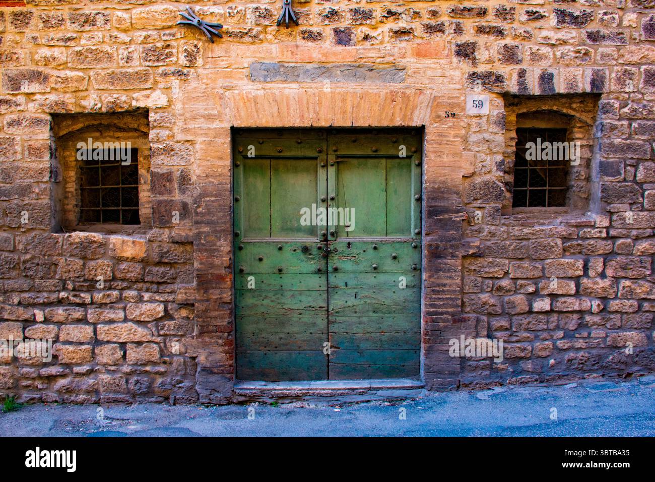 Grüne Holztür mit zwei seitlichen Fenstern in einer mittelalterlichen Stein und Ziegel Wand Stockfoto
