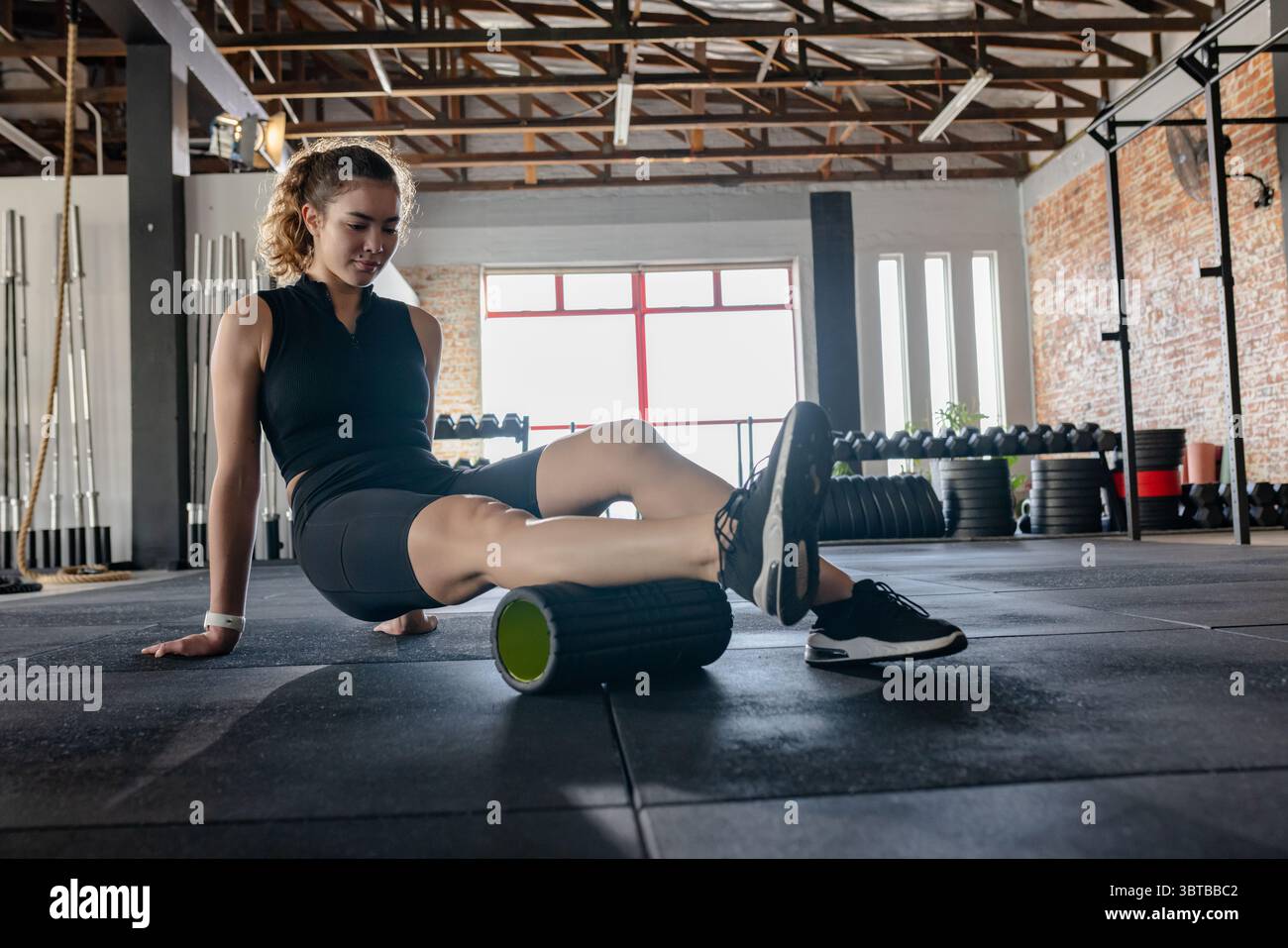 Frau, die den Körper mit der Hand stützt und eine Schaumstoffrolle unter dem Oberschenkel auf dem Fitnessboden verwendet, Kopierraum Stockfoto