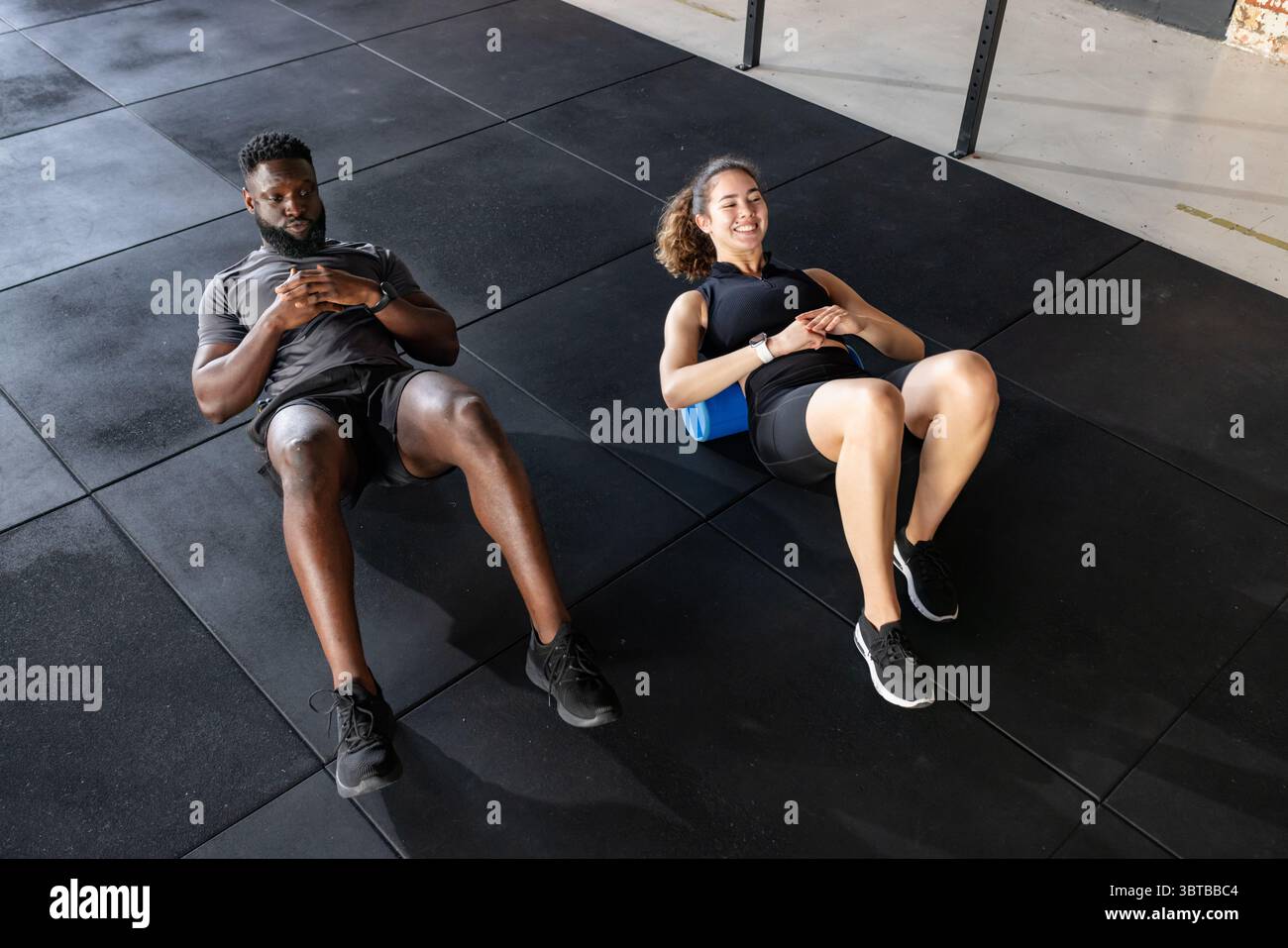 Verschiedene Trainingspartner liegen in Sportbekleidung auf Schaumstoffrollen und trainieren im Fitnessstudio mit Smartwatches Stockfoto
