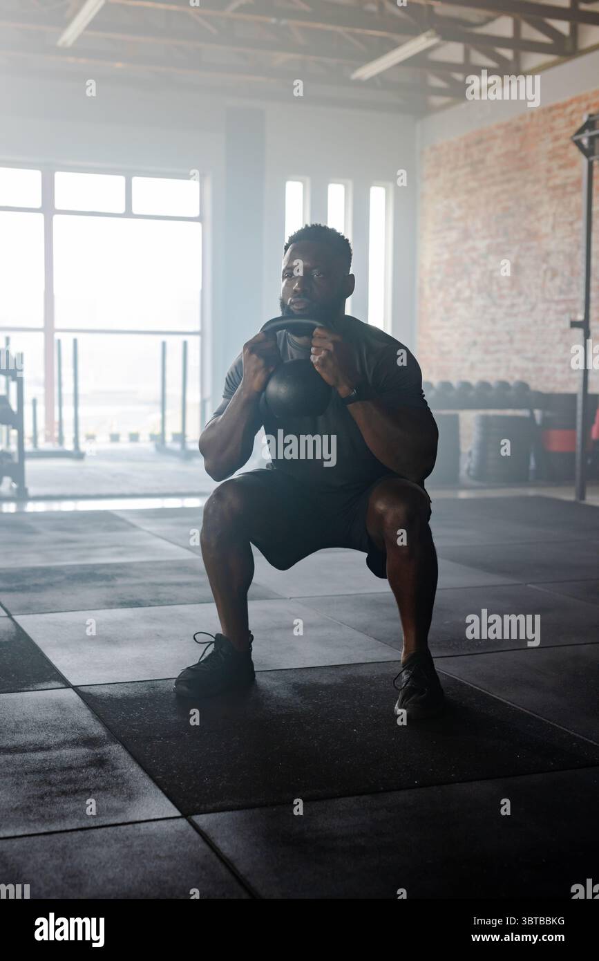 Afroamerikaner in Sportbekleidung, der Kettlebell in der Turnhalle mit Langhanteln und Tellern aufführt Stockfoto
