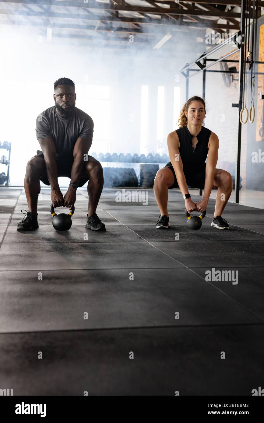 Diverse Trainingspartner hocken im Fitnessstudio mit gelben Kettlebells auf Gummimatten Stockfoto