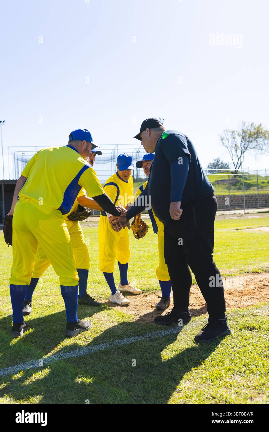 Männliche Baseballspieler und Trainer drängen sich auf dem Feld auf einem Hügel und stapeln Hände mit Uniformen und Handschuhen Stockfoto