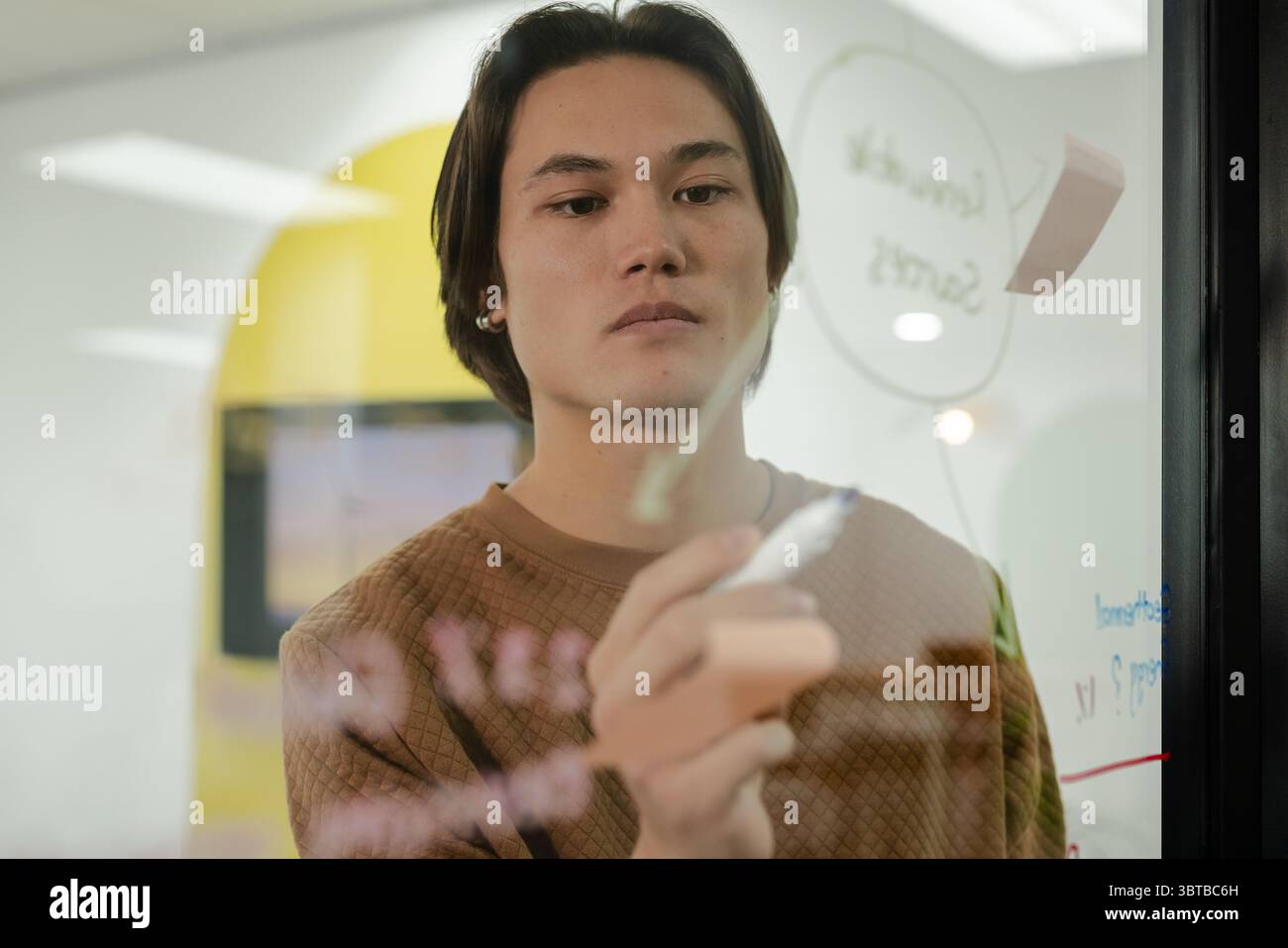 Asiatischer Mann, der kreisförmige Diagramme auf Klarglas-Whiteboard im Büro mit Marker und Haftnotiz zeichnet Stockfoto
