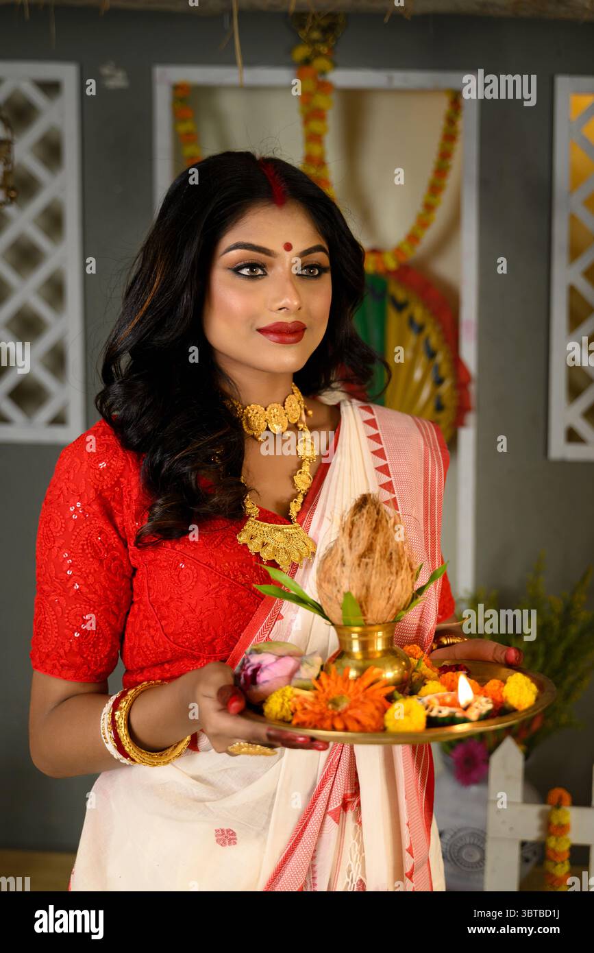 Porträt einer jungen Frau, verziert mit einem traditionellen Saree, ergänzt durch Goldschmuck und Armreifen, mit einem Teller voller religiöser Opfergaben Stockfoto
