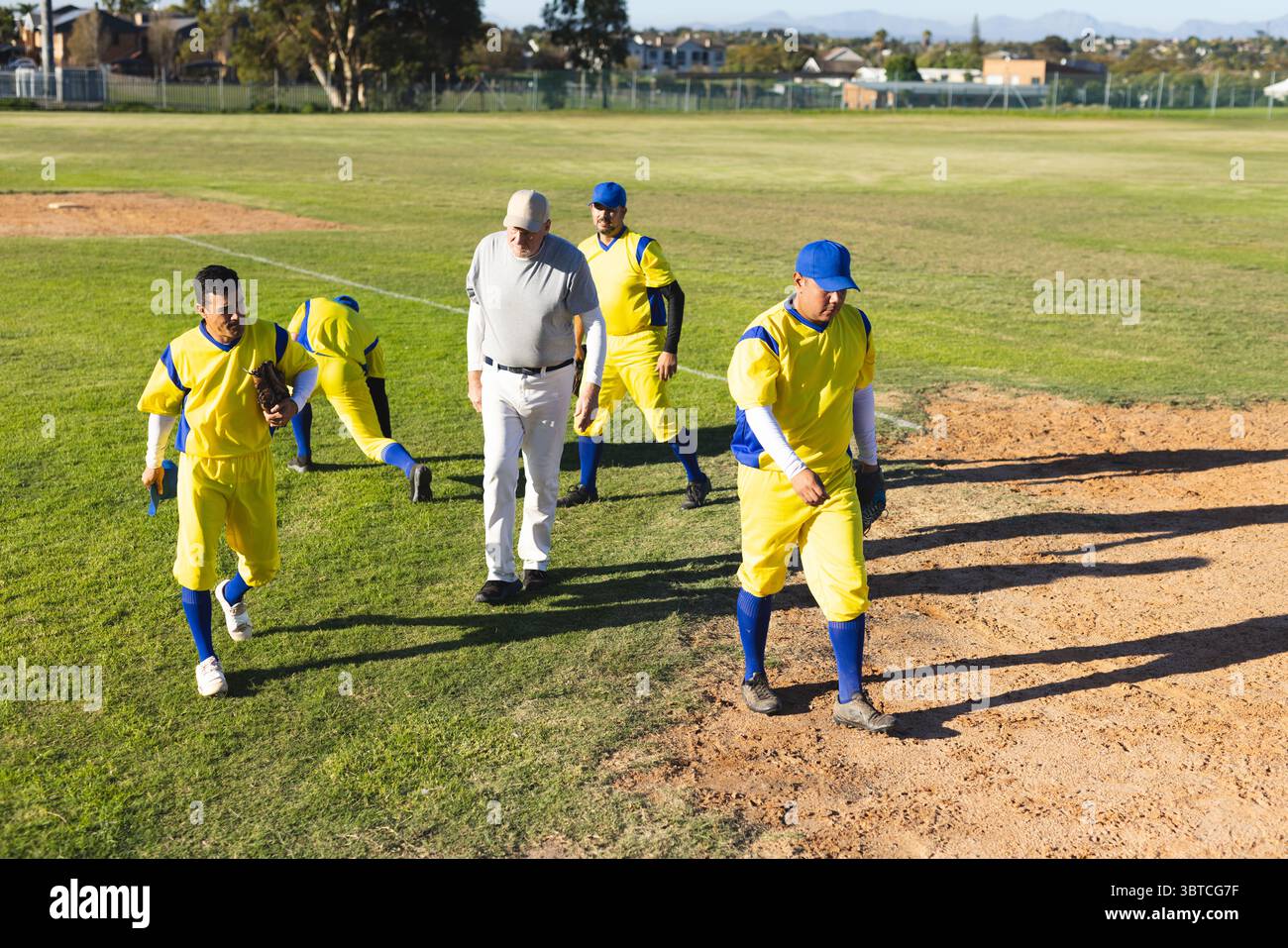Verschiedene männliche Baseballmannschaften mit Trainer, die im Baseballpark Infield überquert haben, in Uniformen und Handschuhen Stockfoto