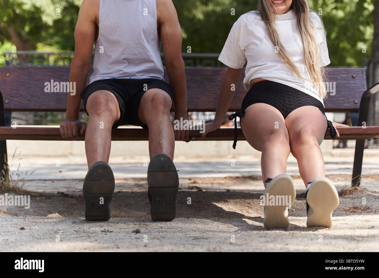 Zwei Fitness-Enthusiasten, die Trizepsdips auf einer Parkbank durchführen und bei einem Outdoor-Workout unter der warmen Sommersonne trainieren Stockfoto