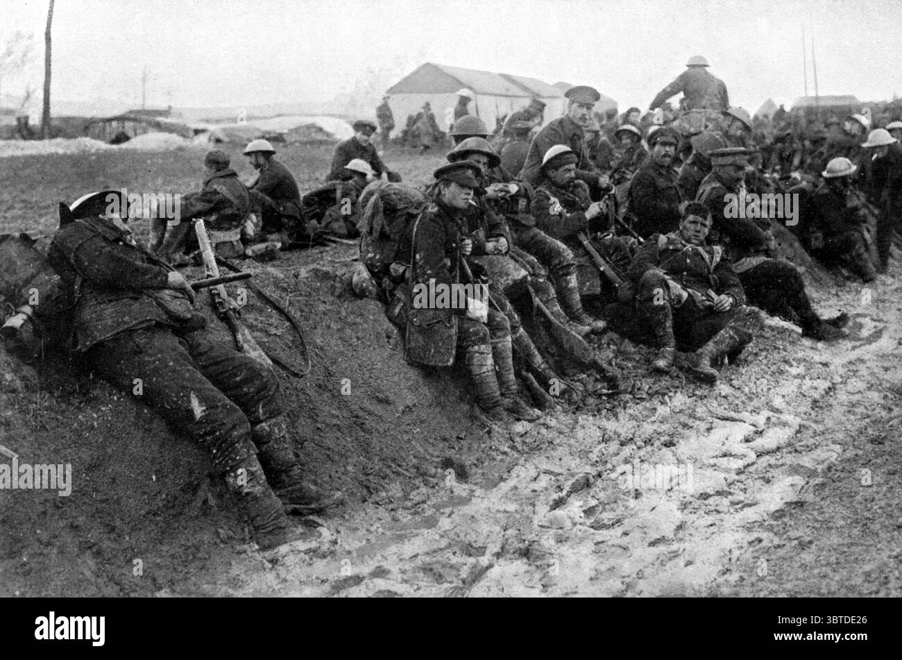 Eine Gruppe von Soldaten des Worcestershire-Regiments ruht auf einem niedrigen Ufer am Rande eines fetten Schlammstroms irgendwo auf dem Schlachtfeld von Somme , Frankreich . Der Mann auf der linken Seite versucht eine Schlummerei , sein rechter Fuß sinkt immer tiefer in das Miry Chaos . Die Infanteristen sehen müde und müde aus. 18. November 1916 Stockfoto